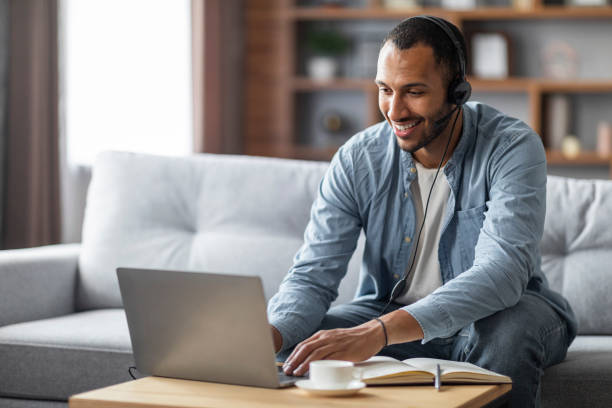 istock Distance Learning. Smiling Black Man In Headset Studying With Laptop At Home 1476001837