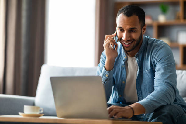 istock Modern Entrepreneurship. Black Man Talking On Cellphone And Using Laptop At Home 1476001857