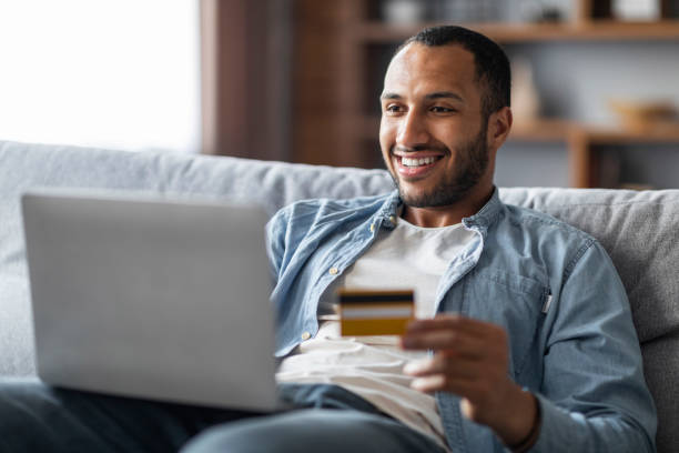 istock Online Shopping. Cheerful Handsome Black Man Using Laptop And Credit Card 1476002021