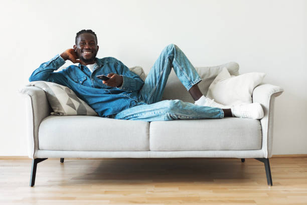 istock Happy Black Guy Watching Television Lying On Sofa At Home 1476002048