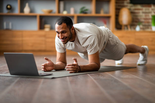 istock Sporty Black Man Training At Home With Laptop, Making Plank Exercise 1476002155