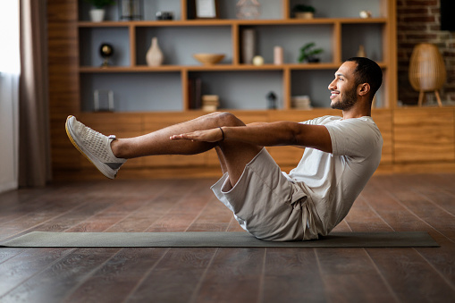 Sporty Young Black Man Making V-Up Abs Workout At Home, Smiling African American Guy Training On Fitness Mat In Cozy Living Room, Enjoying Domestic Workouts And Healthy Lifestyle, Side View