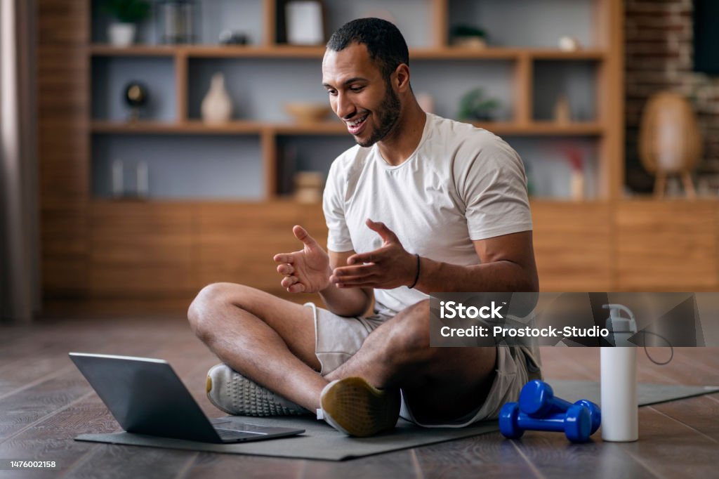 Remote Trainings. Young Black Guy Having Video Call With Sport Coach Remote Trainings. Young Black Guy Having Video Call With Sport Coach, Smiling African American Man Talking At Computer Webcam While Exercising On Fitness Mat In Living Room, Copy Space Coach Stock Photo
