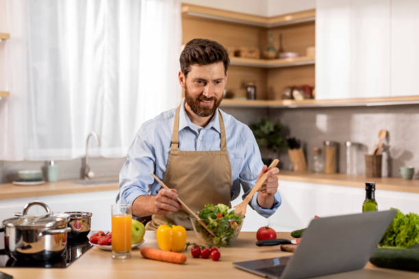 istock Smiling mature caucasian male in apron preparing dinner, watching video lesson on computer 1476002222