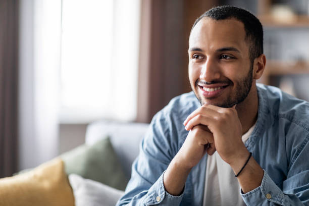 istock Smiling Handsome Black Guy Sitting On Sofa At Home And Looking Away 1476002336