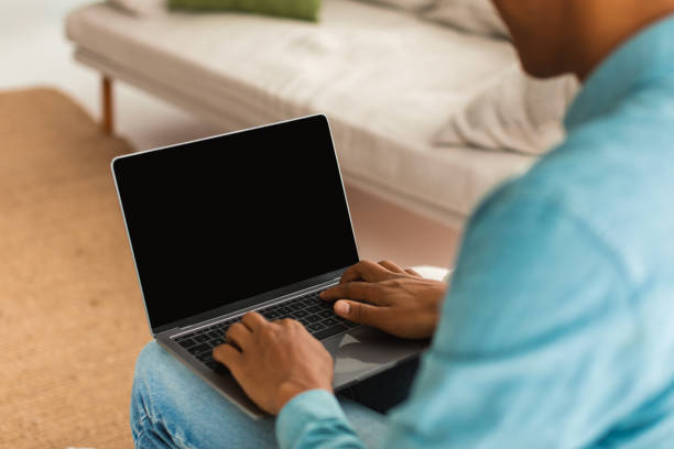 istock Young black guy in jeans typing on laptop with blank screen, chatting remotely in social networks 1476002394