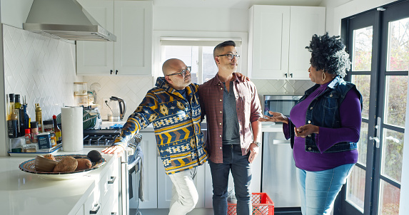 A mixed race gay couple talking to an African American real estate agent inside the kitchen.