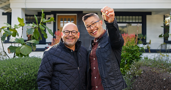 A mixed race gay couple standing outside their new home, showing the key.