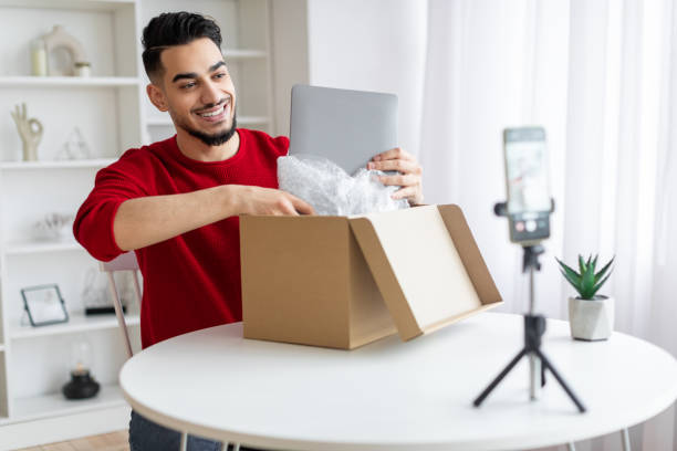 istock Handsome Arab Male Blogger Unboxing Parcel With Laptop On Camera 1476004251