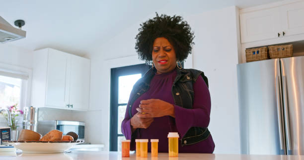 mujer afroamericana mirando sus frascos de pastillas - opening bottle pill bottle pill fotografías e imágenes de stock