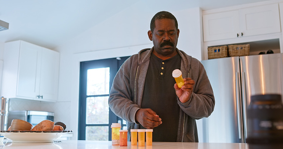 An African American man inspects his pill bottles.