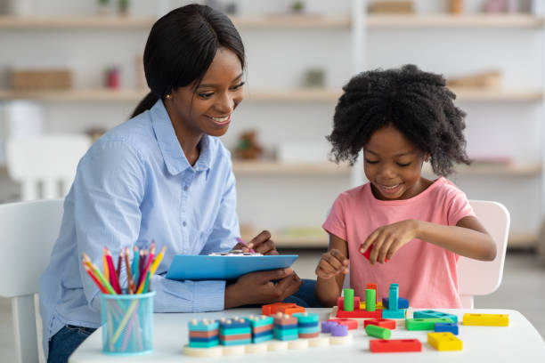 Female psychotherapist working with little kid at office Female psychotherapist friendly pretty young black woman working with little kid at office, sitting by preschooler girl playing with bricks, taking notes and smiling. Child therapist concept animal behavior stock pictures, royalty-free photos & images