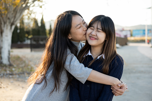 Lifestyle of a young Asian couple reconciling after an anger. One of the girls jumps to hug and kiss the other girl who puts on a face of reluctance, heartbreak, anger.