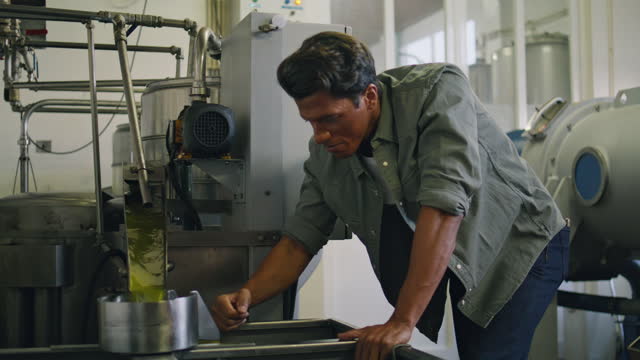 Professional guy tasting olive oil at factory close up. Man controlling process