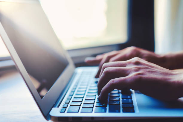 istock Hands of a person operating a laptop near a window 1476016597