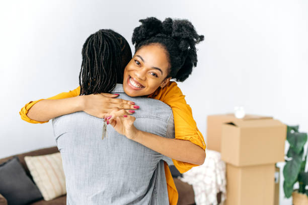 istock Excited joyful african american woman with dreadlocks, hugging her husband while standing in living room, happy female showing keys of their new property, she looking at camera, smiling 1476017823