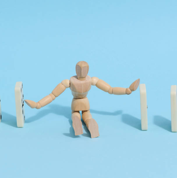 istock A wooden puppet toy holds back a falling domino on a blue background, representing the concept of a strong personality 1476019380
