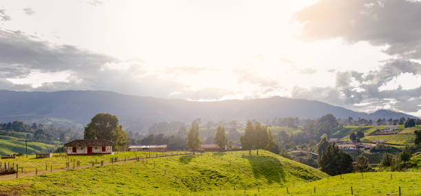 A serene landscape of lush green hills dotted with quaint farmhouses and distant mountains, all illuminated by the warm glow of the setting sun