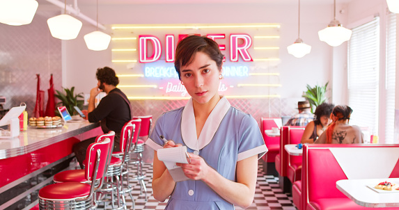 A POV shot of a waitress taking an order in a 1950s styled diner.