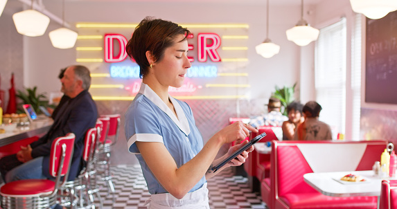A POV shot of a waitress using a tablet in a 1950s styled diner.