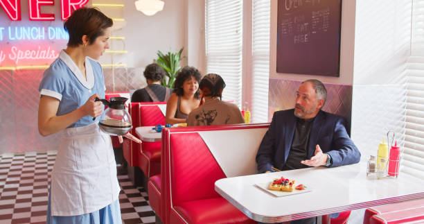 istock Waitress Holding Coffee Pot Talking To Customer In 1950s Styled Diner 1476022818