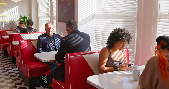 A small group of customers sitting in booths in a 1950s styled diner.