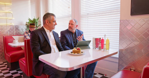 istock Two Men In Suits Talking To Each Other In 1950s Styled Diner 1476023438