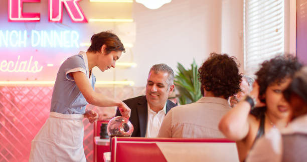 Waitress Pouring Coffee For Customers In 1950s Styled Diner