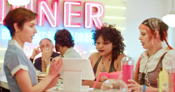 istock Waitress Showing Tablet To Two Non-Binary People In 1950s Styled Diner 1476023481