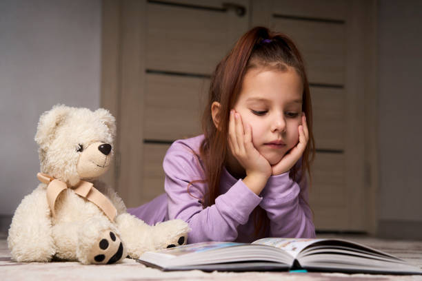 istock Cute girl lying on the floor and reading a book 1476028128