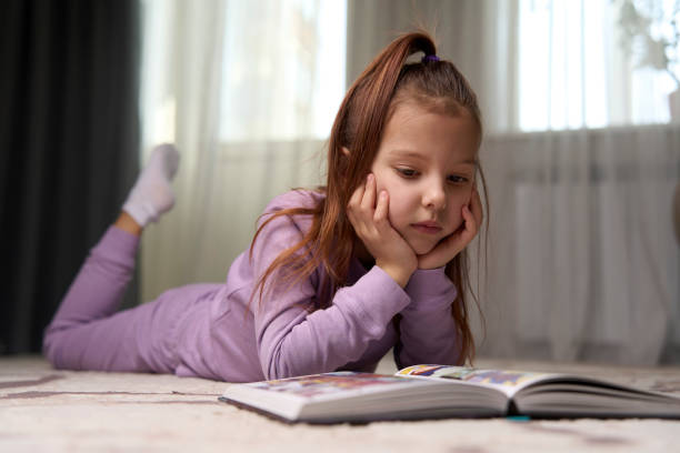istock Cute girl lying on the floor and reading a book. 1476028133