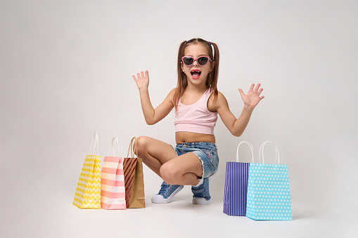 Cute little girl with shopping bags on a white background with copy space. Portrait of a child girl with colorful shopping bags, full body