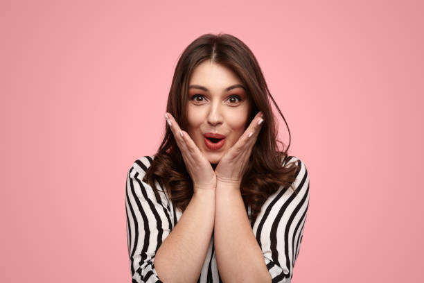 istock Surprised young lady shouting and touching cheeks against pink background 1476041496