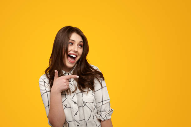 Portrait of a beautiful young woman pointing with her finger while standing in front of a bright yellow background.