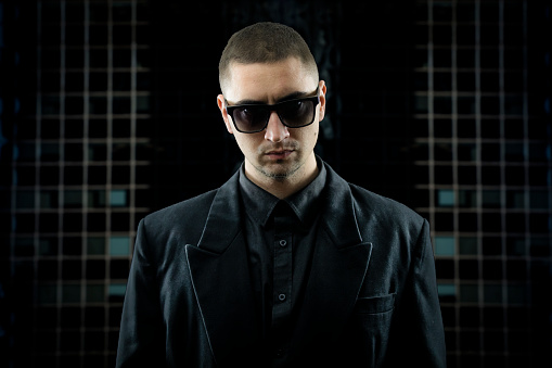 Studio Shot of Young Man in Black Suit and Sunglasses Looking at Camera.