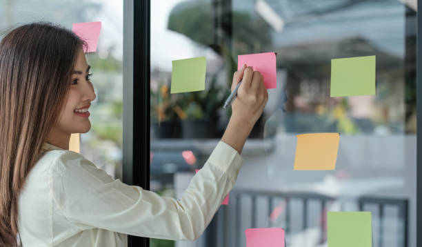 istock Businesswoman using sticky notes in glass wall while holding coffee cup to writing strategy. 1476064869