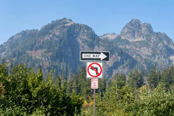 Photo of Road signs: One way, No parking any time, forbidden left turn, on the mountain background