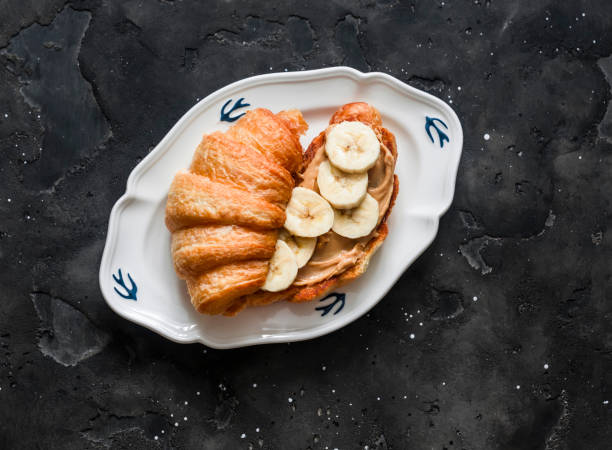 Croissant sandwich with peanut butter, banana on a dark background, top view