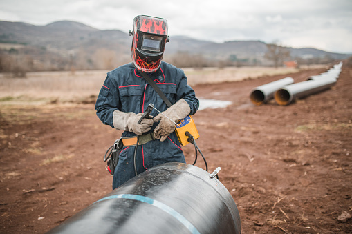 A welder with protective equipment, gloves and a mask, prepares to weld pipes