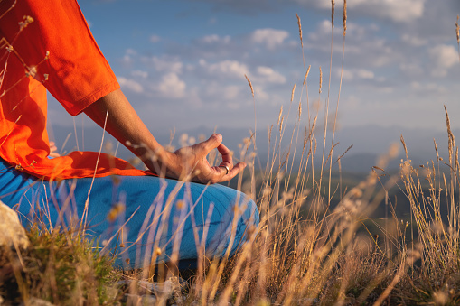 Close-up of a peaceful woman meditating while sitting in the mountains in the grass, an exercise in calmness and balance.