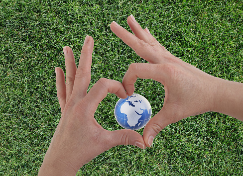 Planet in heart shape hands on grass background