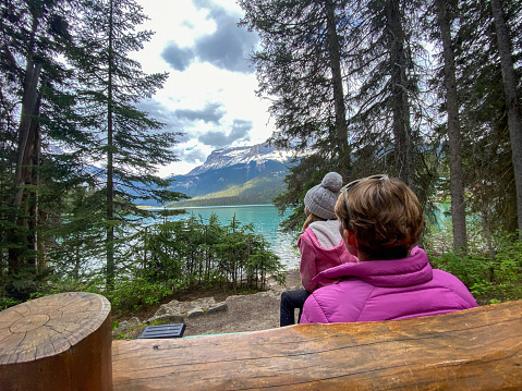 Mother and daughter sit and enjoy the views over the pristine mountain lake. Family vacation visiting Emerald Lake in Canada