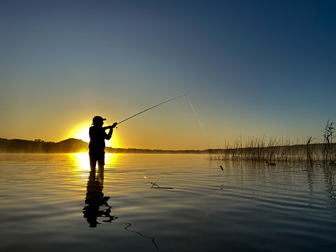 A young boy enjoys fishing for bass early in the morning while on vacation.