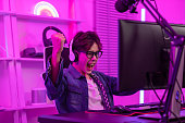 Asian gamer with a happy expression and raised fists in front of a computer screen,Celebrating winning a online video game. Professional gamer concept
