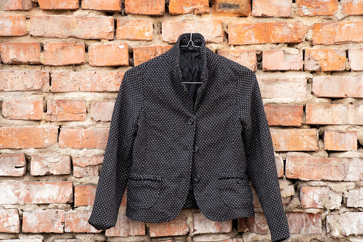 black womens blazer with polka dots hanging on a brick old wall outside in the sun
