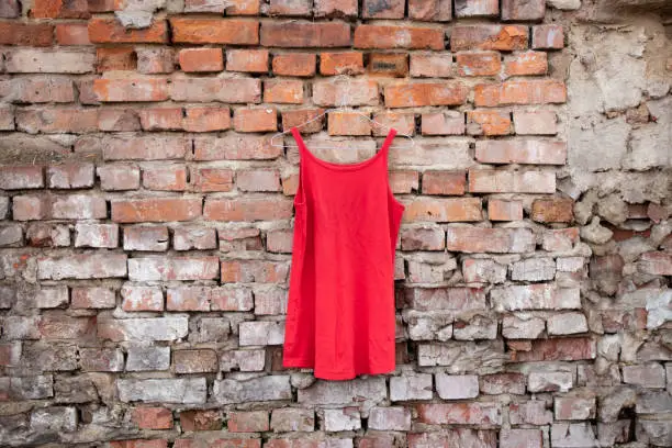 Photo of red womens dress hanging on a brick old wall outside