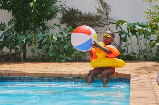 Ball, play or kid in swimming pool in summer relaxing on fun holiday vacation or weekend at home backyard. Happiness, swimming or healthy African child floating or playing water games for exercise