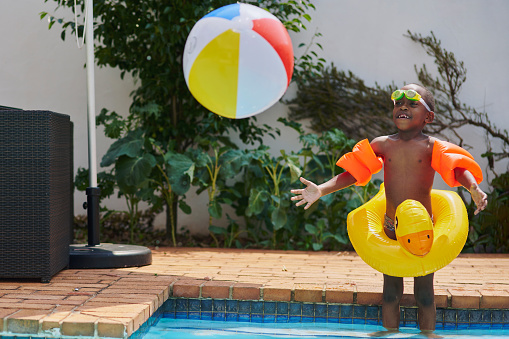 Swimming, black child in pool throwing ball with smile and fun time in water with toys in backyard in summer. Swim, play and sun, boy with beachball and happy, safe activity for young kids on weekend