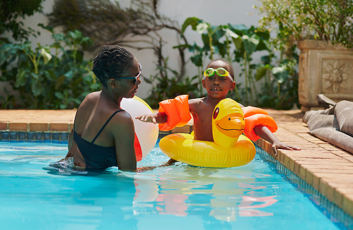 Black family, mother and child learning swimming in pool, having fun and bonding together. Love, education and mama, woman or mom teaching kid or boy how to swim in water and enjoying holiday time.
