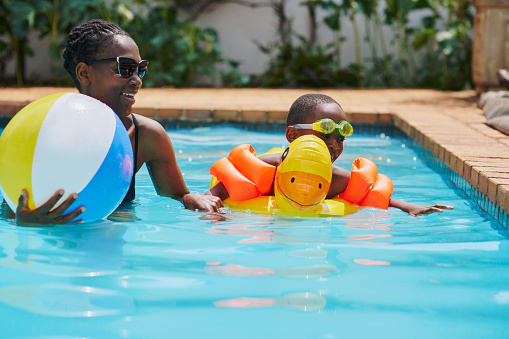 Mother, black family and child learning swimming in pool, having fun and bonding together. Love, education and happy mama or mom teaching kid or boy how to swim in water and enjoying holiday time.